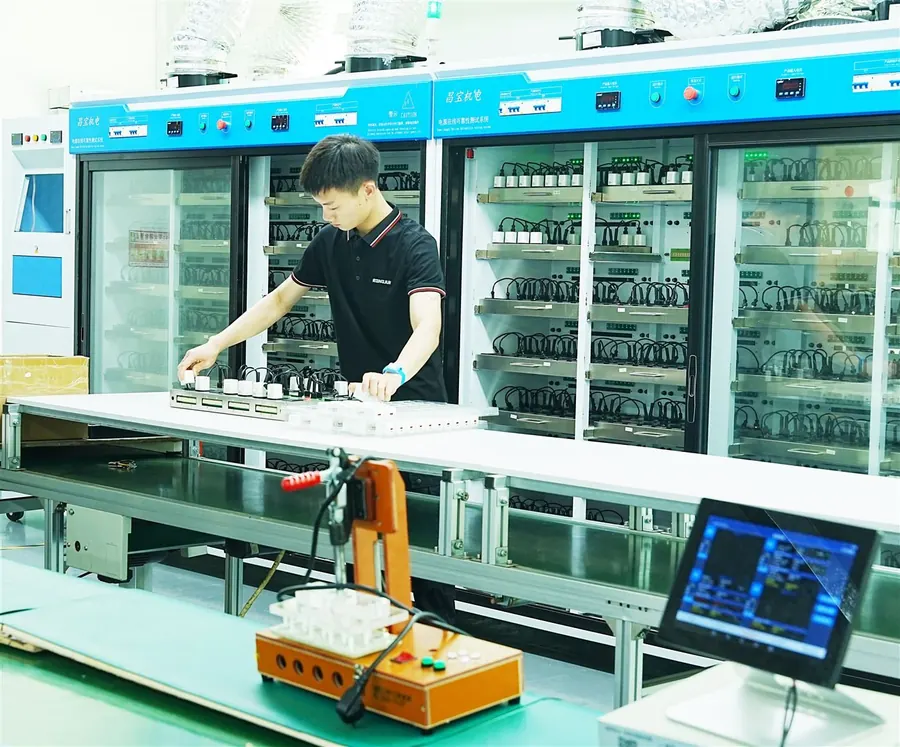 Aging test racks with GaN chargers running under load and a technician at the test bench
